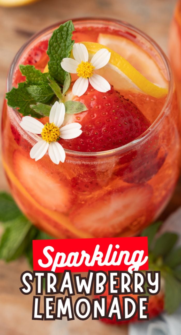 A glass of sparkling strawberry lemonade with ice, fresh strawberries, lemon slices, mint, and small white flowers creates a refreshing twist on classic strawberry lemonade.