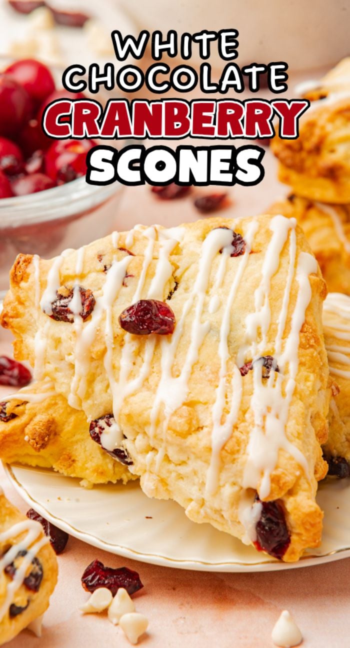 A white chocolate cranberry scone with icing on a plate, cranberries and chocolate chips nearby—an easy scone recipe perfect for anyone seeking a delicious fresh cranberry recipe.