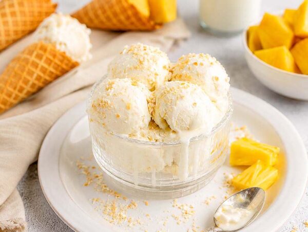 Four scoops of vanilla ice cream in a bowl with pineapple chunks and waffle cones on the side, perfect for those who love frozen yogurt ice cream or want to make froyo at home.