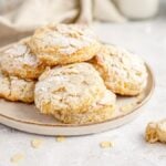A plate of almond cookies dusted with powdered sugar, with a bitten cookie beside the plate—try pairing these treats with scones made with pineapple for a delightful twist on your afternoon spread.