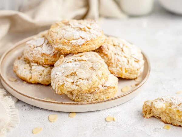 A plate of almond cookies dusted with powdered sugar, with a bitten cookie beside the plate—try pairing these treats with scones made with pineapple for a delightful twist on your afternoon spread.