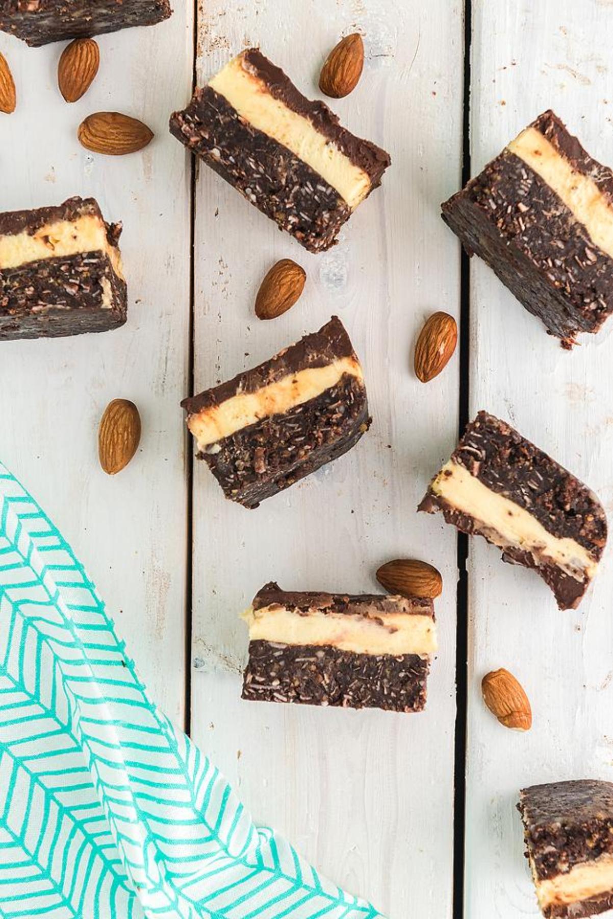 Classic Canadian dessert: Chocolate and cream layered bars with whole almonds rest on a white wooden surface beside a green striped cloth—perfect for anyone seeking an easy layered bar recipe.
