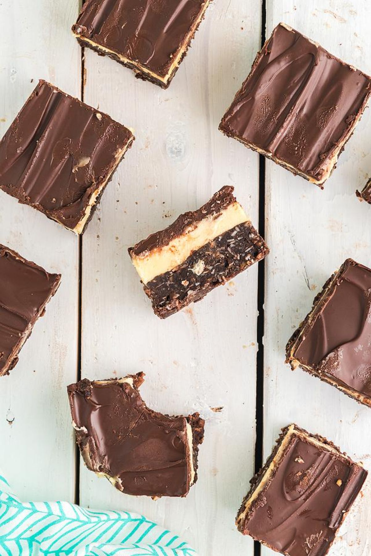 Squares of classic Canadian Nanaimo bars on a white wooden surface, with one layered bar revealing its creamy middle layer.