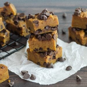 Pumpkin chocolate chip bars stacked and scattered on parchment and a cooling rack, these pumpkin squares with chocolate chips make the perfect cozy treat.