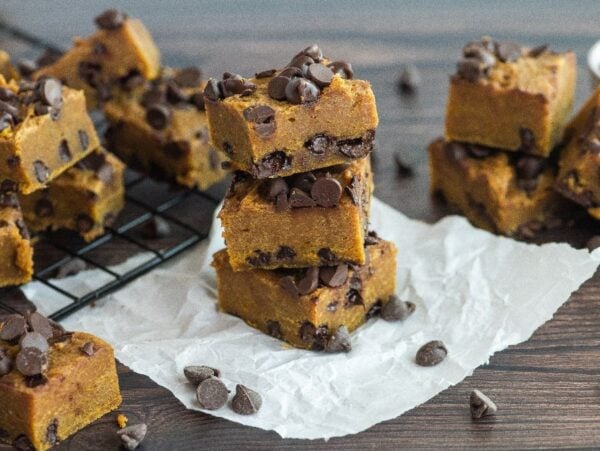 Pumpkin chocolate chip bars stacked and scattered on parchment and a cooling rack, these pumpkin squares with chocolate chips make the perfect cozy treat.