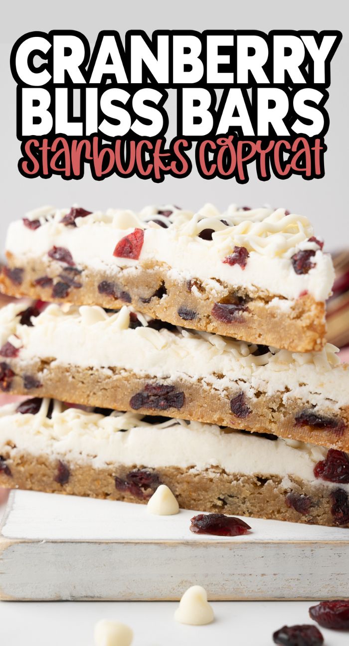 Three homemade bliss bars with white frosting and cranberries, stacked on a board—a Starbucks copycat cranberry bliss bars recipe.