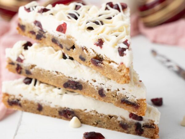 Three stacked Starbucks copycat cranberry bliss bars with creamy topping sit on a white surface—these easy cranberry bars are the perfect homemade bliss bars for any dessert lover.