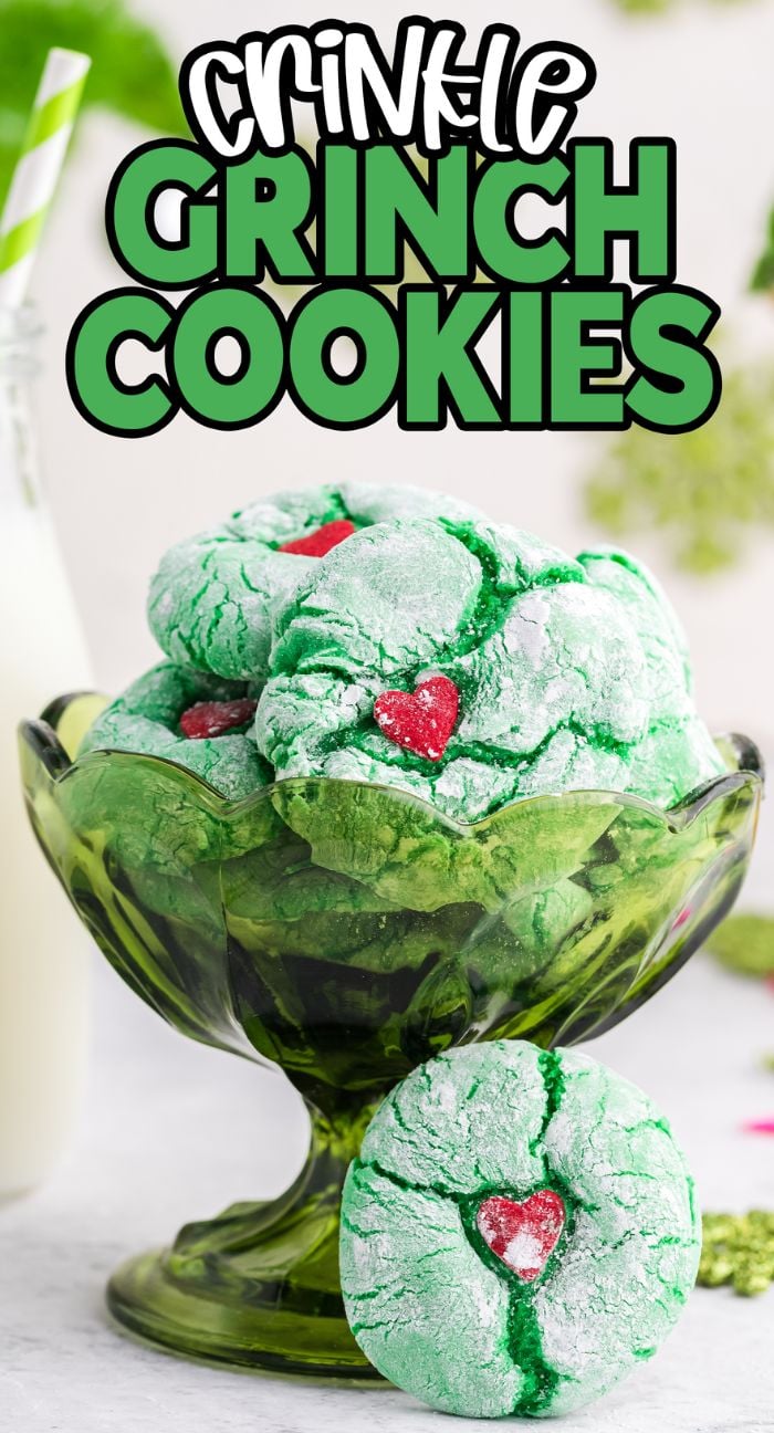A green glass bowl filled with Crinkle Grinch Cookies—green crinkle cookies with a red heart in the center. These easy cake mix cookies are perfect for grinch Christmas cookie trays!.