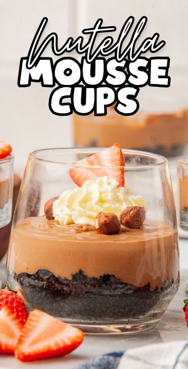 A glass cup with Nutella mousse, whipped cream, hazelnuts, and sliced strawberries on top—these Nutella mousse cups are a delightful treat for any dessert lover.