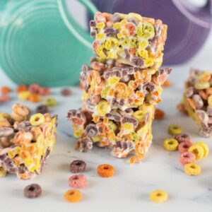 Three stacked fruit loops squares with scattered colorful cereal pieces on a white surface.
