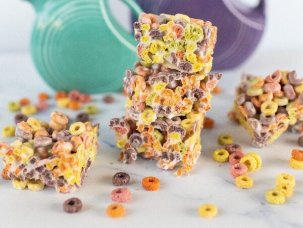 Three stacked fruit loops squares with scattered colorful cereal pieces on a white surface.