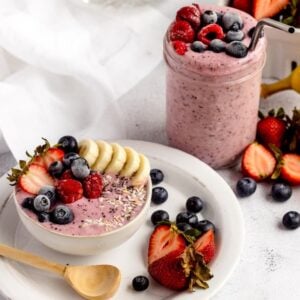 Smoothie bowl and smoothie jar topped with berries and banana, surrounded by fresh fruit on a white table—perfect inspiration for DIY Meal Prep or creating your own homemade smoothie pack for quick, healthy breakfasts.