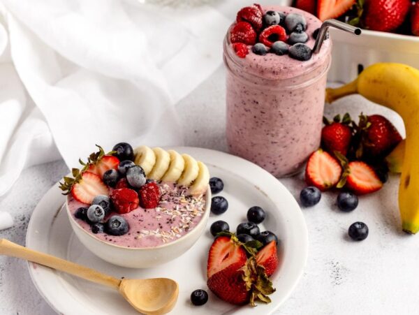 Smoothie bowl and smoothie jar topped with berries and banana, surrounded by fresh fruit on a white table—perfect inspiration for DIY Meal Prep or creating your own homemade smoothie pack for quick, healthy breakfasts.