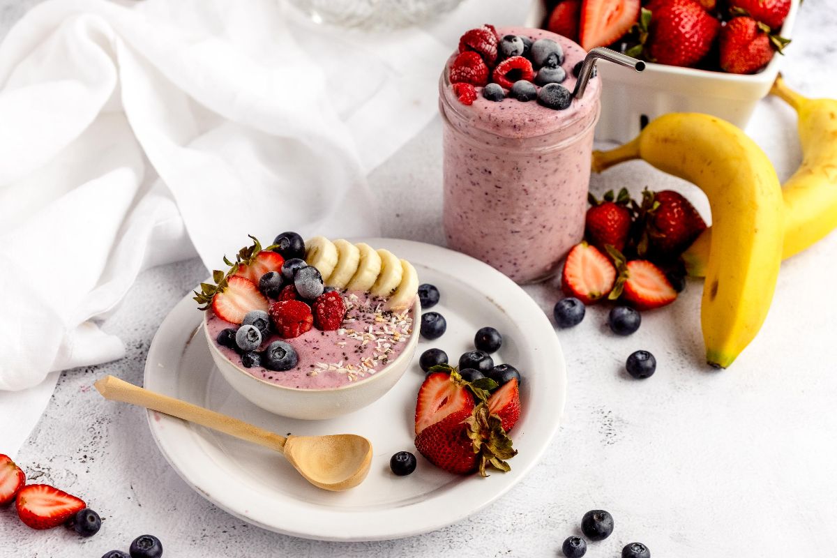 Smoothie bowl topped with bananas, berries, and seeds, alongside a berry smoothie jar, banana, and strawberries—perfect for DIY Meal Prep or using your favorite homemade smoothie pack.
