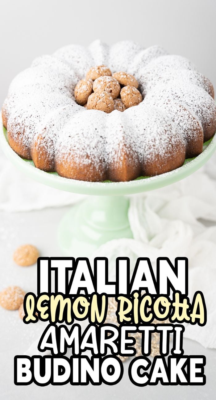 A powdered sugar-covered Lemon ricotta amaretti cake, topped with amaretti cookies, is displayed on a green cake stand.