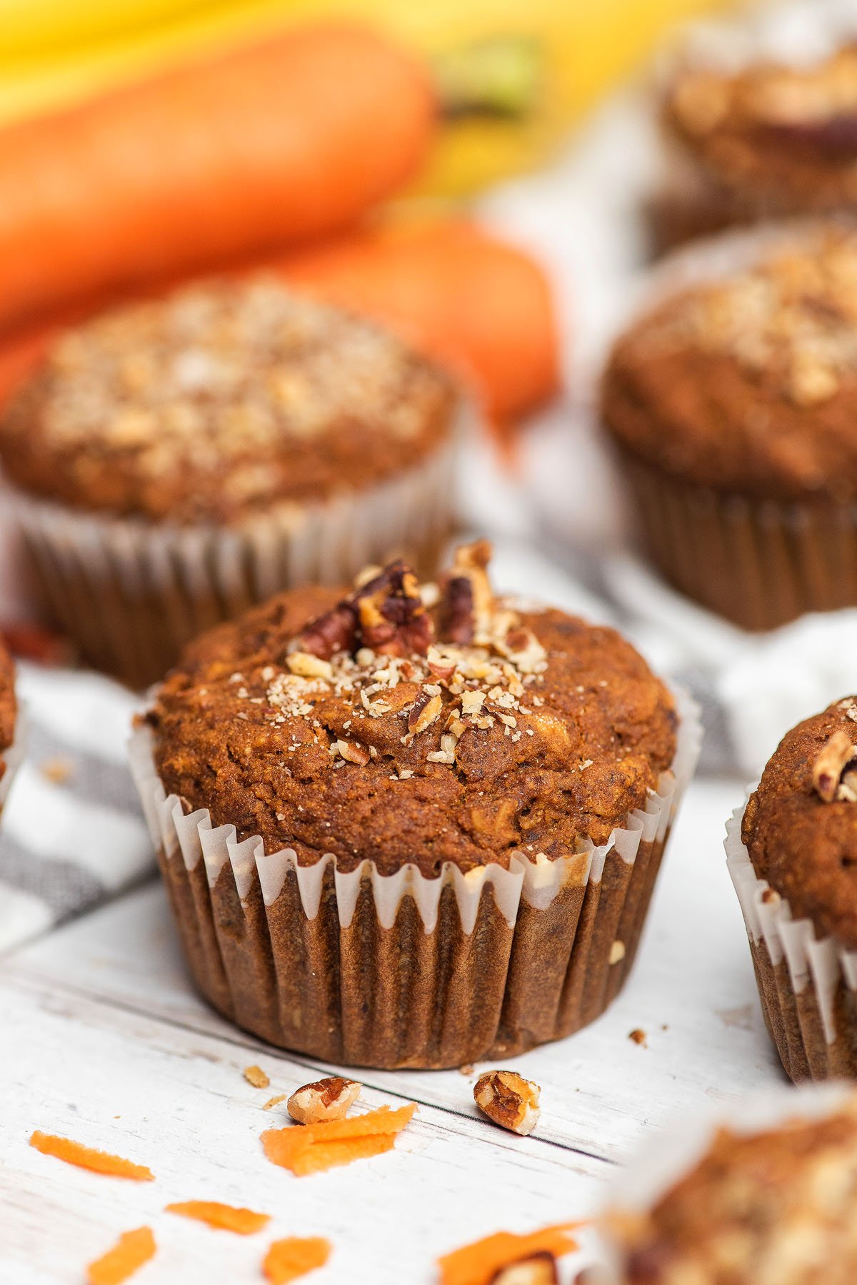 Close-up of Morning Glory Muffins with chopped nuts on top, with fresh carrots in the background—perfect gluten free muffins for a wholesome treat.