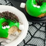 Green monster donuts with candy eyes and chocolate sprinkles on a skeleton hand plate—a spooky baked Halloween donut that looks like a Frankenstein monster, perfect for your Halloween donut decorating fun.