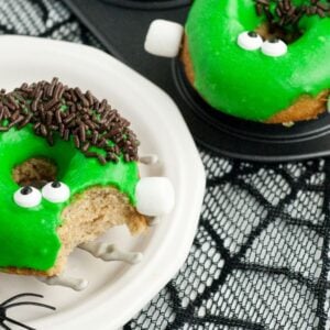 Green monster donuts with candy eyes and chocolate sprinkles on a skeleton hand plate—a spooky baked Halloween donut that looks like a Frankenstein monster, perfect for your Halloween donut decorating fun.