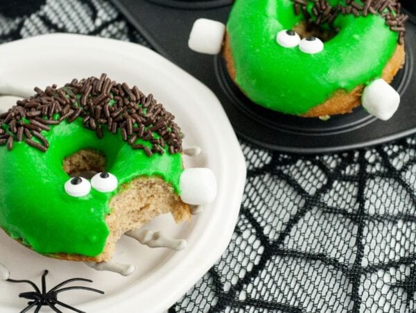Green monster donuts with candy eyes and chocolate sprinkles on a skeleton hand plate—a spooky baked Halloween donut that looks like a Frankenstein monster, perfect for your Halloween donut decorating fun.