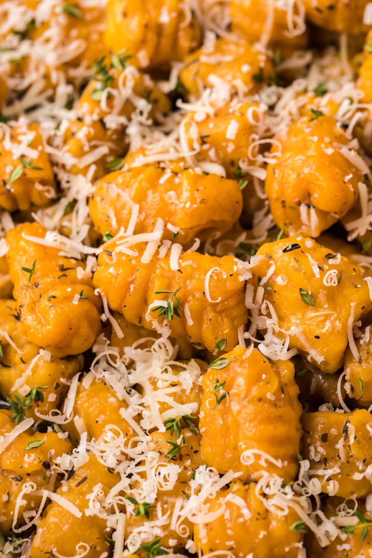 Close-up of sweet potato gnocchi topped with grated cheese, herbs, and black pepper, served with a rich roasted garlic sauce.