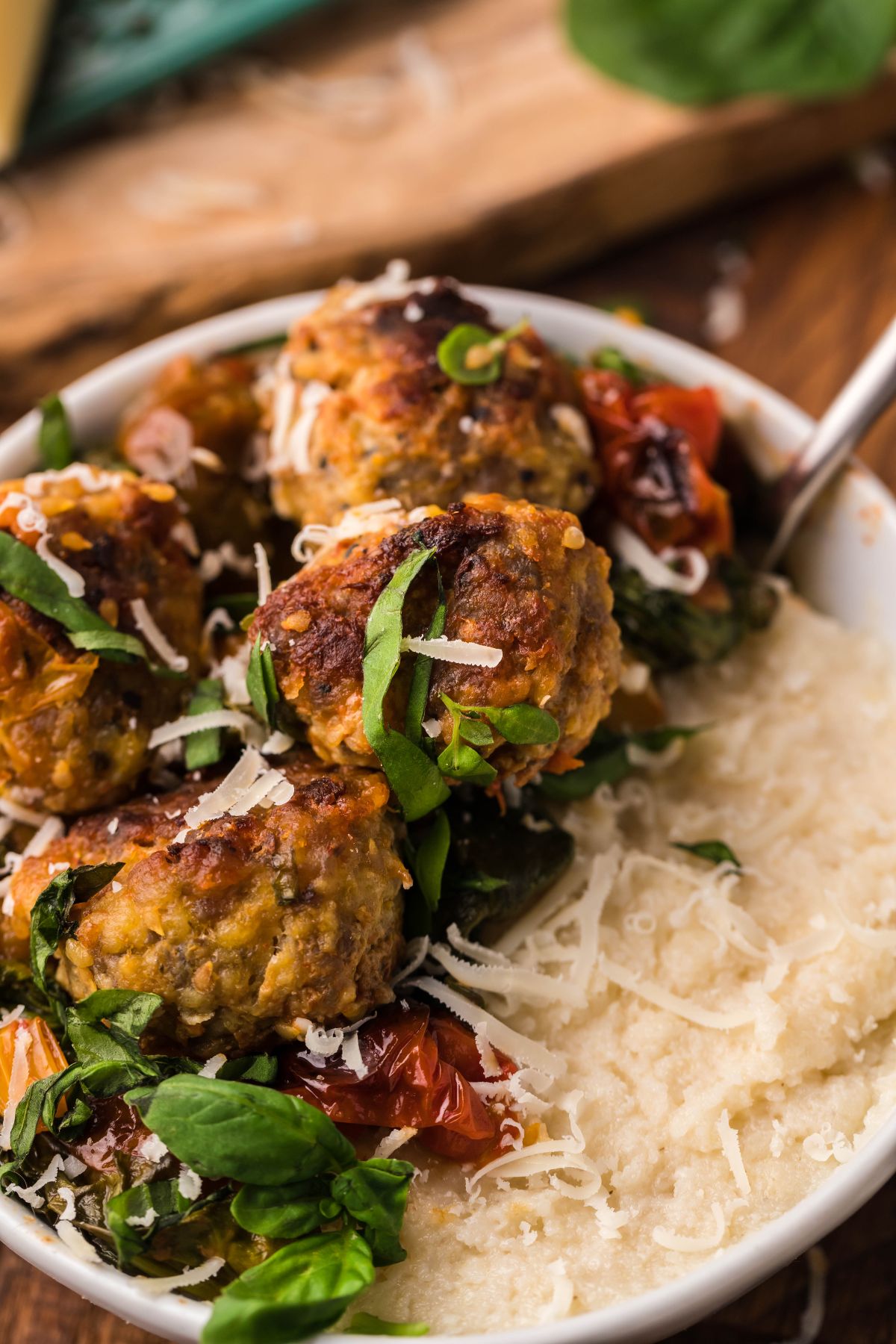 Enjoy this Roasted Tomato and Meatball Polenta—a delicious Italian meatball dinner idea with juicy meatballs, tomato, spinach, and cheese over creamy polenta served in a white bowl.