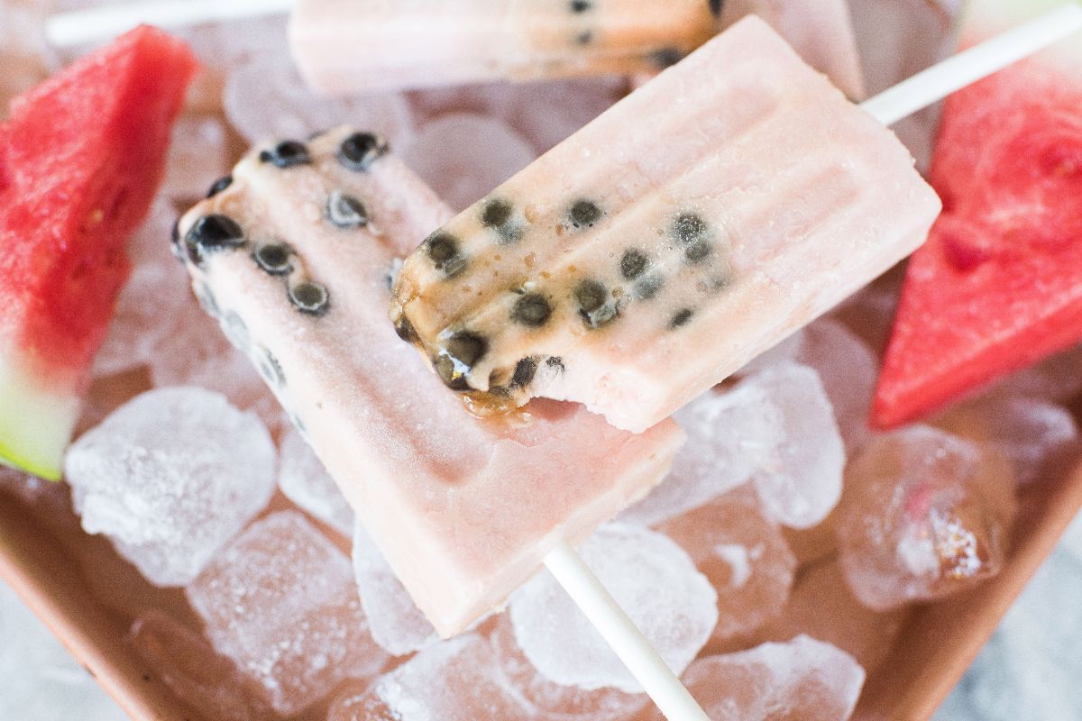 Watermelon boba popsicles with black seeds rest on ice, surrounded by slices of watermelon.