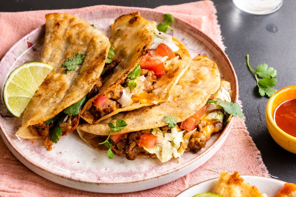 Three crispy turkey tacos filled with meat, lettuce, tomato, and cilantro, served with lime on a plate—a quick and easy dinner perfect for taco lovers.