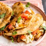 Three crispy turkey tacos filled with meat, lettuce, tomato, and cilantro, served with a lime wedge and salsa on the side—a quick and easy dinner inspired by our favorite turkey taco recipe.