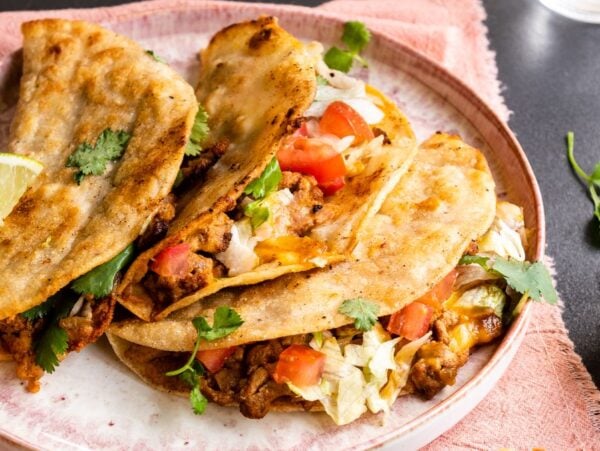 Three crispy turkey tacos filled with meat, lettuce, tomato, and cilantro, served with a lime wedge and salsa on the side—a quick and easy dinner inspired by our favorite turkey taco recipe.