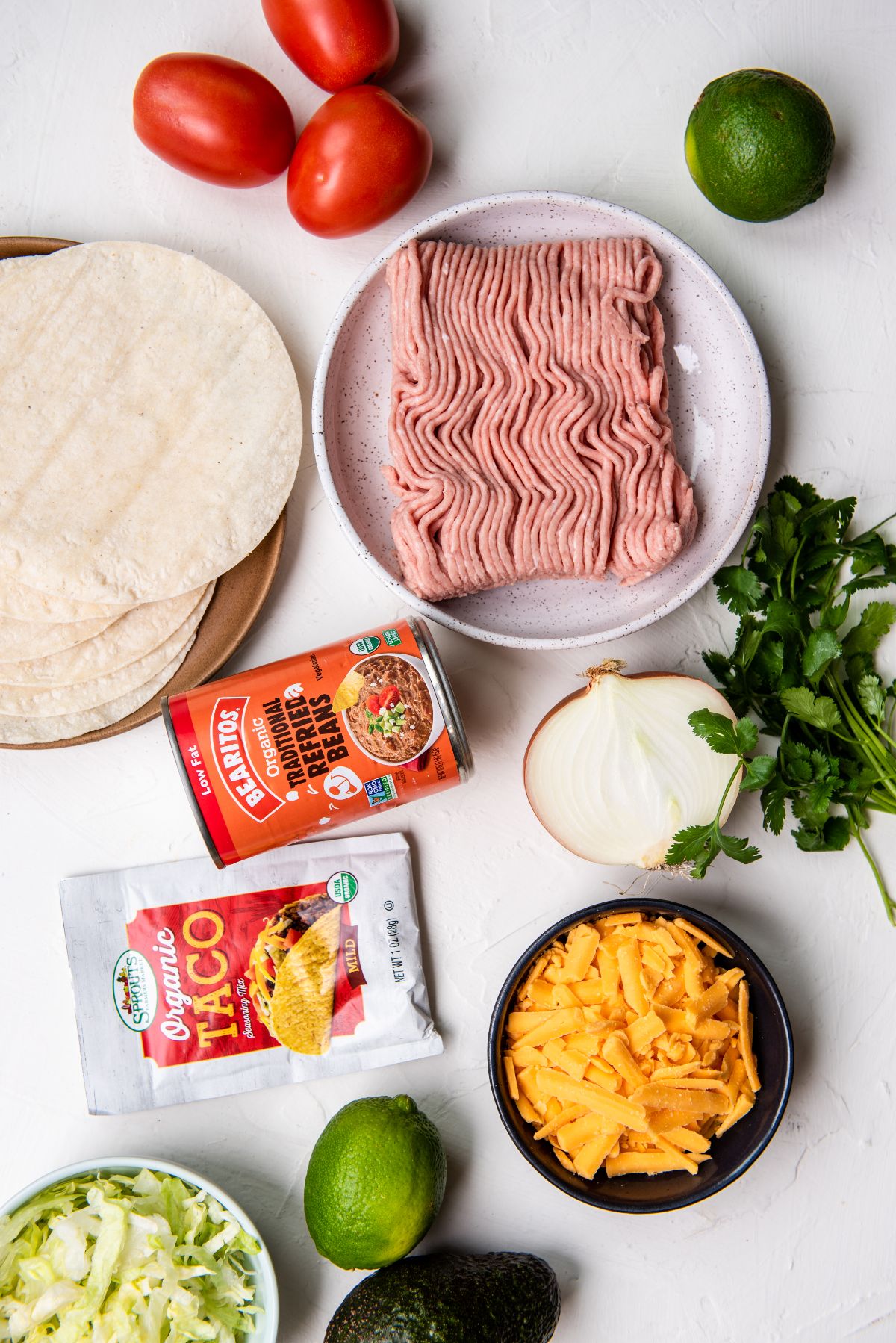 Taco ingredients: ground meat, tortillas, tomatoes, cheese, onion, lettuce, lime, cilantro, avocado, taco mix—try this as a delicious turkey taco recipe or learn how to make a crispy taco with ground turkey.