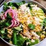 A vibrant Elote Corn Kale Salad bowl with greens, grilled corn, sliced avocado, pickled onions, cheese, and cilantro—a fresh twist on the classic Mexican elote and a delicious kale salad recipe.
