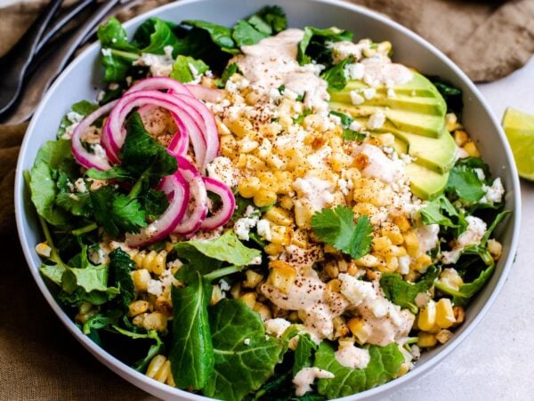 A vibrant Elote Corn Kale Salad bowl with greens, grilled corn, sliced avocado, pickled onions, cheese, and cilantro—a fresh twist on the classic Mexican elote and a delicious kale salad recipe.