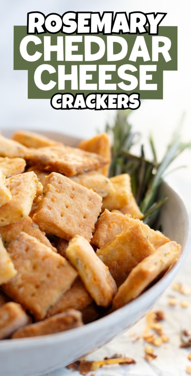 A bowl of square rosemary cheddar cheese crackers made from a homemade cracker recipe, with sprigs of rosemary in the background.