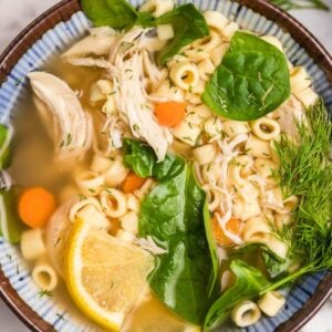 A bowl of Greek lemon chicken soup with spinach, carrots, a lemon slice, and fresh dill—perfect for those craving an authentic recipe for chicken avgolemono soup.