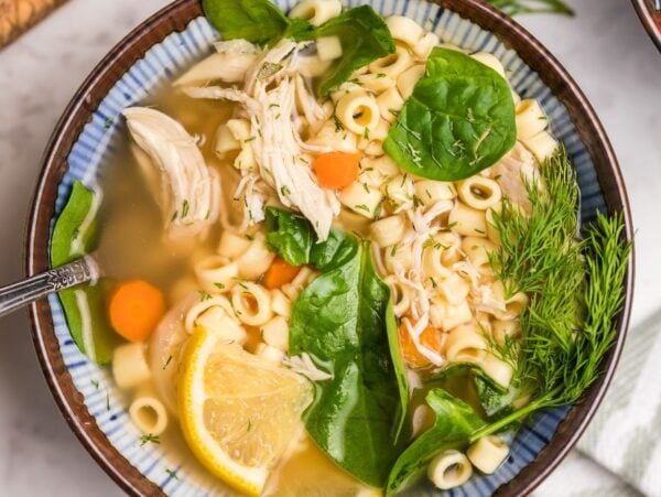 A bowl of Greek lemon chicken soup with spinach, carrots, a lemon slice, and fresh dill—perfect for those craving an authentic recipe for chicken avgolemono soup.