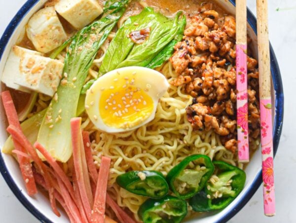 Bowl of ramen with egg, tofu, bok choy, ham, jalapeños, minced meat, and chopsticks on the side—perfect for fans of Spicy Chicken Miso Ramen or anyone craving ramen with chicken and tofu.