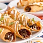 Three beef taquitos topped with sour cream and herbs on a white plate, with more taquitos in the background—an easy air fryer taquitos dish perfect for a gluten free Mexican dinner.