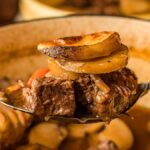 A spoonful of beef with sliced potatoes and carrots captures the essence of a hearty beef and potato one pot meal, simmering perfectly in its own flavors.