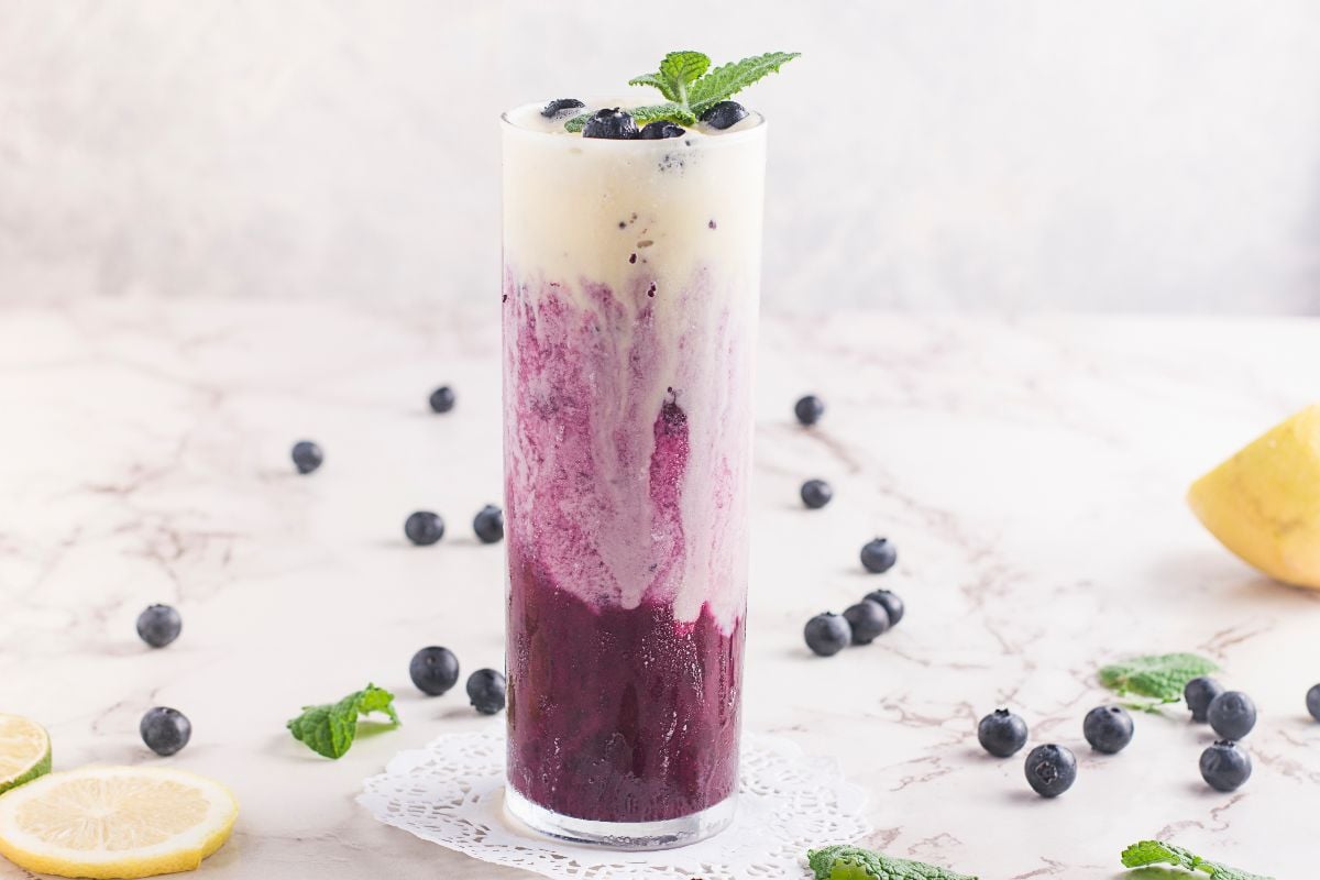 Enjoy a refreshing blueberry ice cream float—an iced, layered blueberry and cream drink in a tall glass, garnished with mint and blueberries.