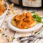 Chicken curry on naan without yeast, with rice, naan, and cilantro, served beside cutlery and a slow cooker.