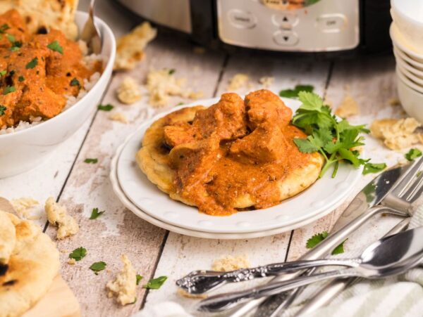 Chicken curry on naan without yeast, with rice, naan, and cilantro, served beside cutlery and a slow cooker.