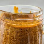 Close-up of a glass pitcher filled with frothy dalgona coffee on a light background, perfect alongside homemade unagi or as a refreshing pairing with sauce for seafood.