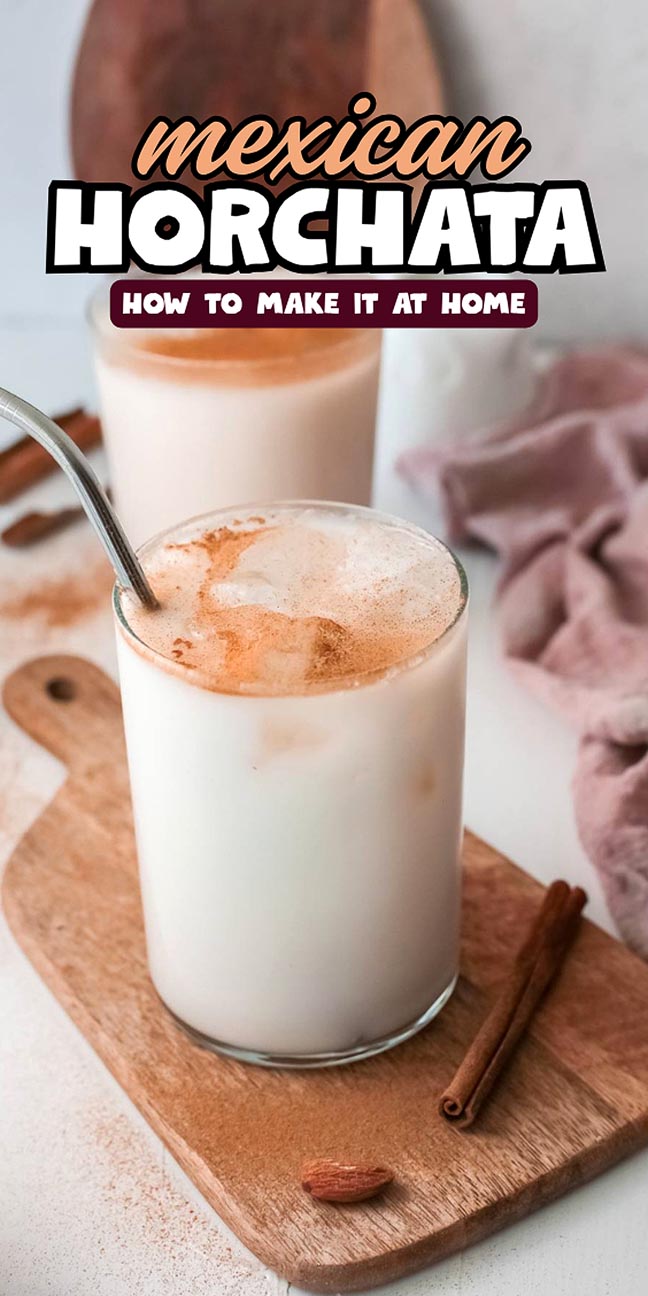 A glass of horchata with ice and cinnamon, on a wooden board, with another glass in the background.