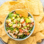 A bowl of seafood ceviche recipe featuring fresh shrimp, diced avocado, and vegetables, surrounded by tortilla chips on a plate.