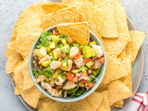 A bowl of seafood ceviche recipe featuring fresh shrimp, diced avocado, and vegetables, surrounded by tortilla chips on a plate.