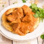 Chunks of curry-spiced meat over flatbread on a white plate, garnished with fresh cilantro—a delicious Chicken curry recipe that's perfect as an easy slow cooker recipe.