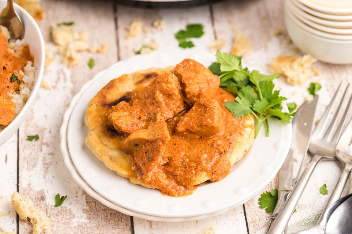 A plate of naan bread topped with creamy slow cooker butter chicken curry, garnished with fresh cilantro.