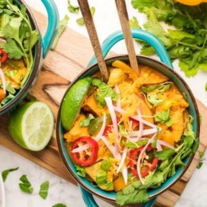 Two bowls of colorful curry, inspired by a hearty Thai recipe with chicken, loaded with veggies, lime wedges, herbs, and sliced chili peppers on a marble surface.