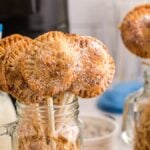 Mini s’mores pie pops dusted with powdered sugar in mason jars, with milk in bottles and striped straws nearby—a sweet twist inspired by the air fryer s’more recipe.