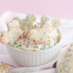 Bowl of funfetti Dunkaroo dip with colorful sprinkle cookies shaped like teddy bears on a pink background.